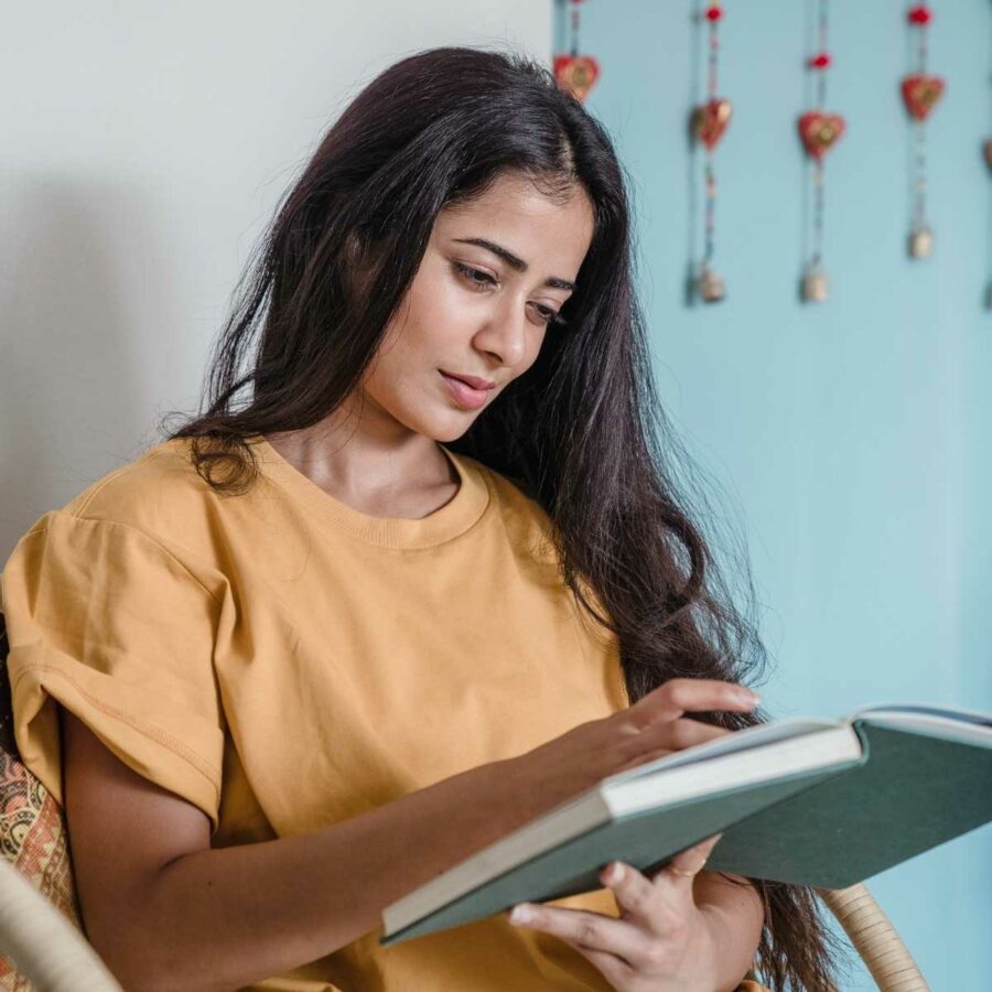 A woman intently reading a book with a blue cover.